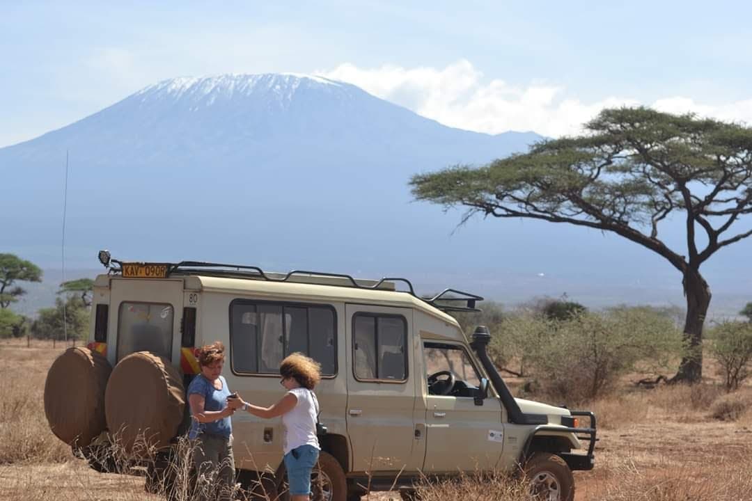 Guests standing beside a safari Land Cruiser with snow-capped Kilimanjaro behind