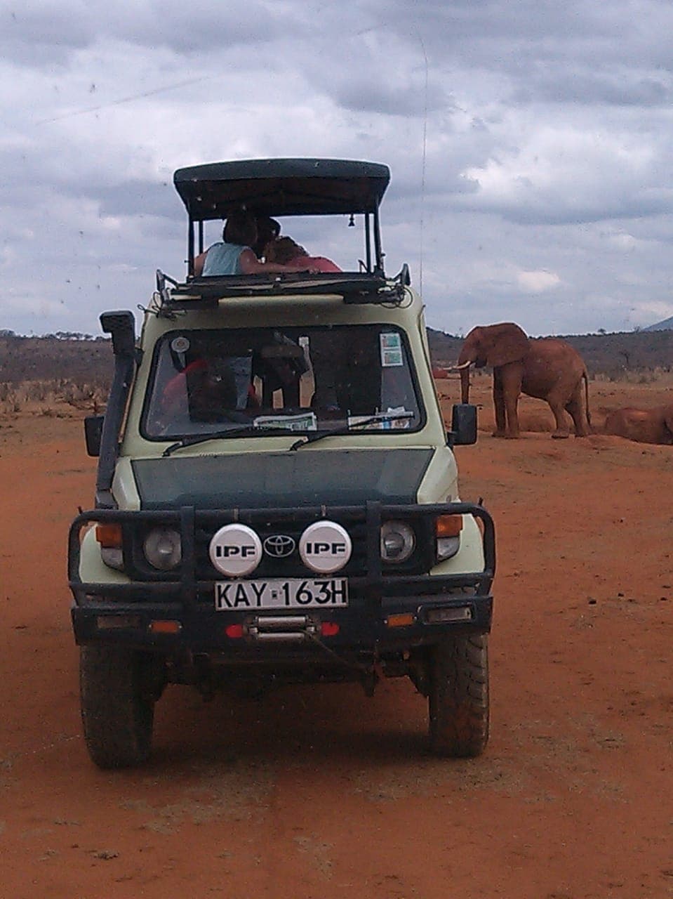 Guests in the pop-up roof of a Tsavo Trails Land Cruiser with an elephant behind